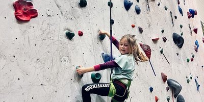 Jente som klatrer på klatrevegg.