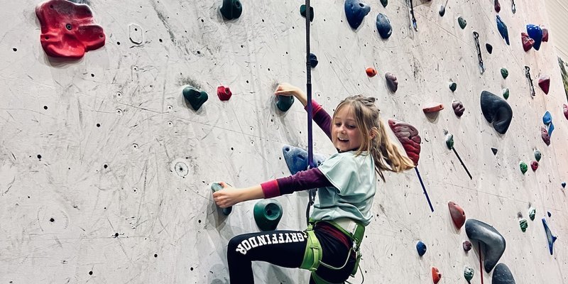 Jente som klatrer på klatrevegg.