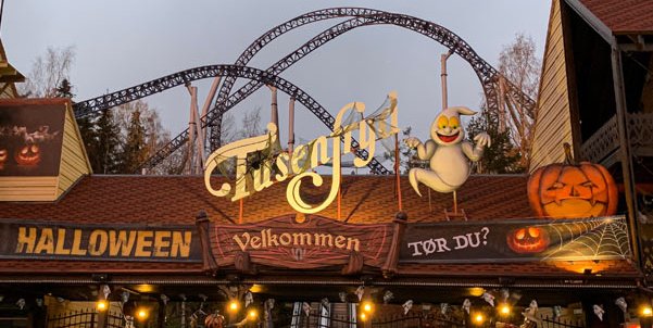 Inngangen til Tusenfryd pyntet til Halloween. Over porten står det «Tusenfryd Velkommen», flankert av et stort smilende spøkelse og et gresskar. På skiltene står det «HALLOWEEN» og «Tør du?». I bakgrunnen sees berg- og dalbanen mot en grå himmel.